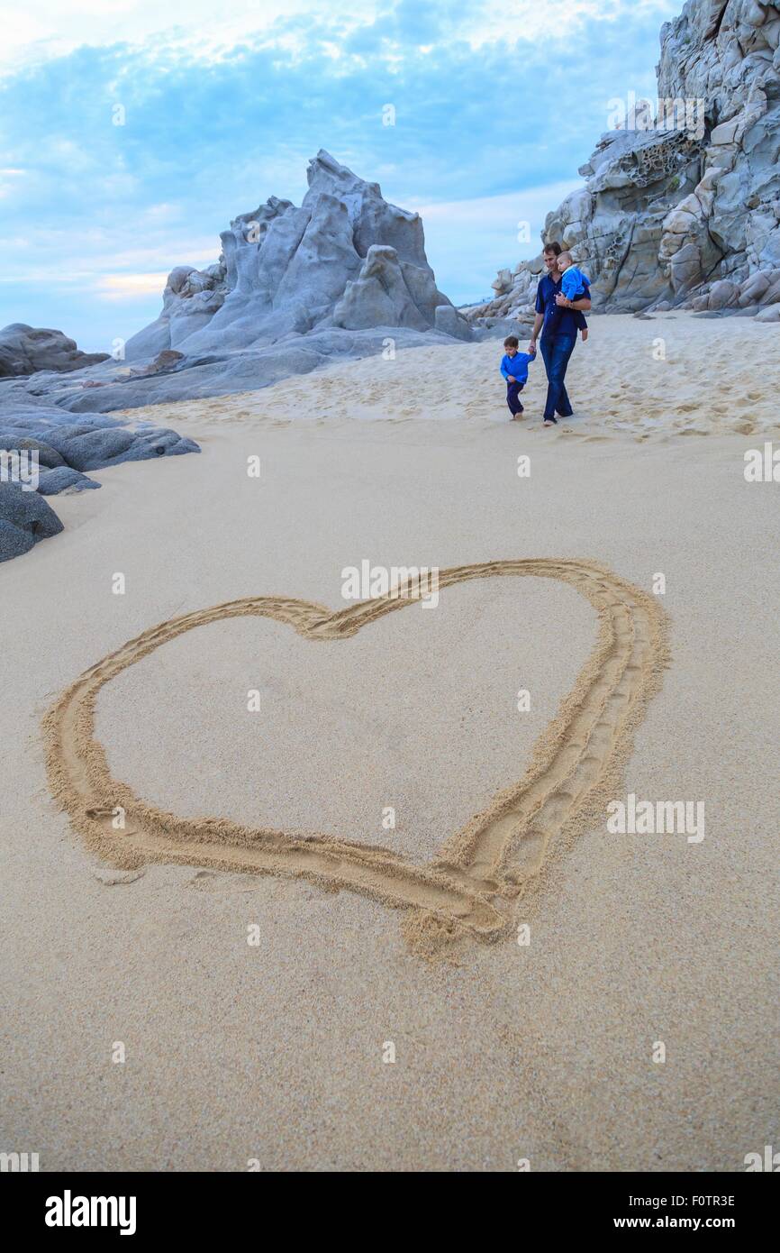 Vater und Söhne zu Fuß am Strand, Herzform im Vordergrund Stockfoto