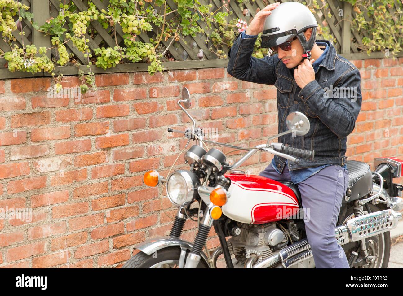 Mitte erwachsener Mann, sitzend auf dem Motorrad, Helm aufsetzen Stockfoto