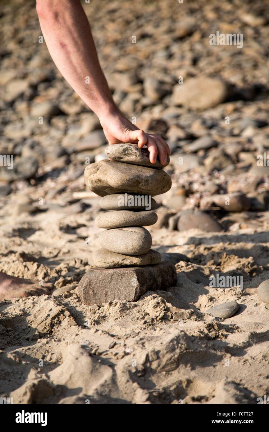 Hand des jungen Mannes platzieren Stein auf Stein Stapel am Strand Stockfoto
