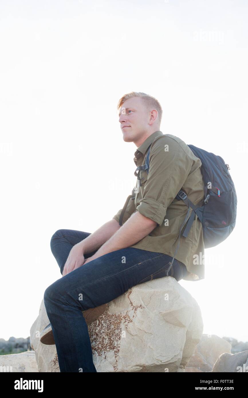 Junger Mann mit Rucksack sitzt auf Fels wegschauen Stockfoto