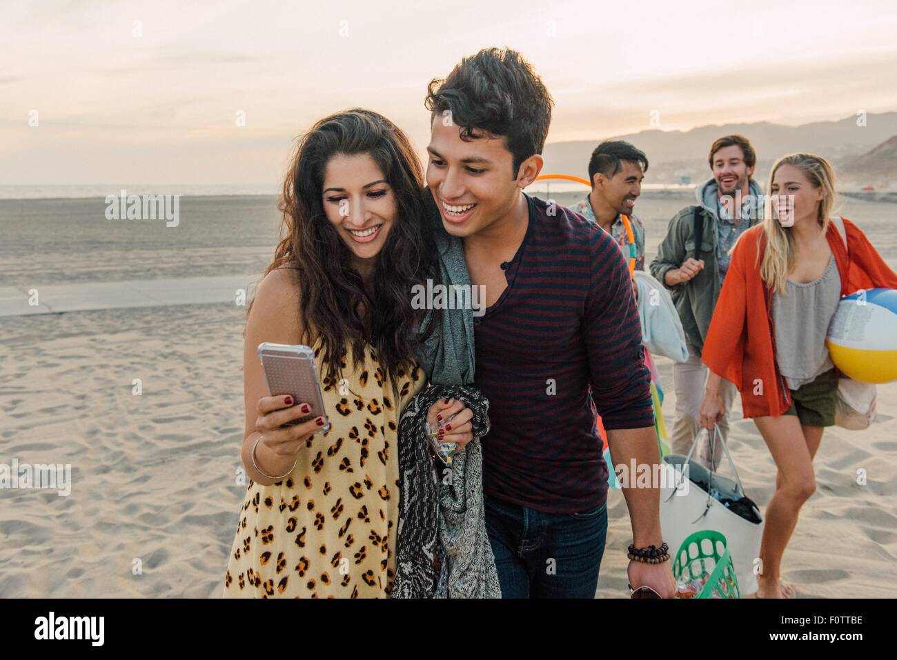 Gruppe von Freunden zu Fuß am Strand, junge Paar Smartphone betrachten Stockfoto