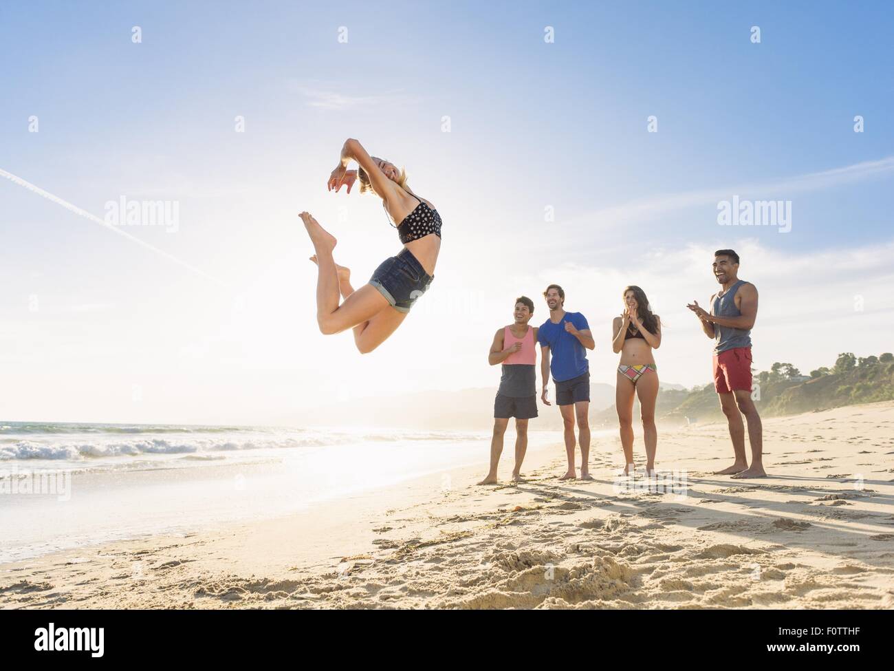 Gruppe von Freunden am Strand beobachten Freund Sprung in der Luft Stockfoto