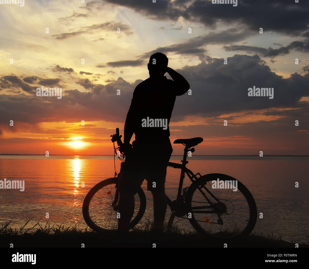 Silhouette eines Mannes mit dem Mountainbike am Ufer Flusses bei Sonnenuntergang Stockfoto