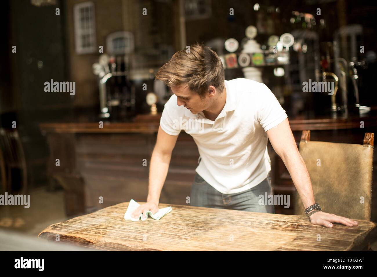 Junger Mann Reinigung Tisch im Wirtshaus Stockfoto