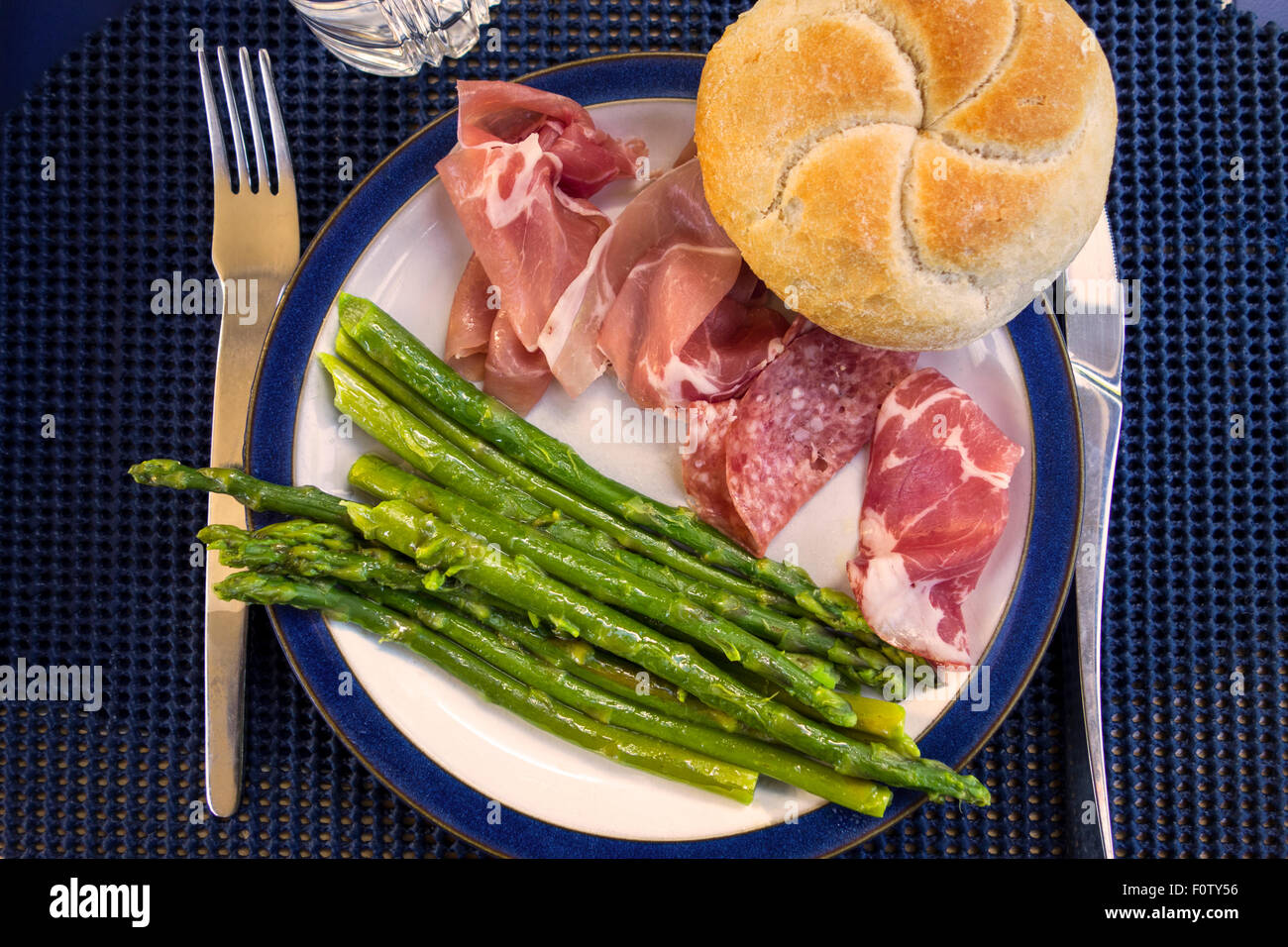 Ein Teller mit italienischen Antipasti Fleisch (Schinken, Salami Milano, Coppa) mit Spargel und ein Brötchen Stockfoto
