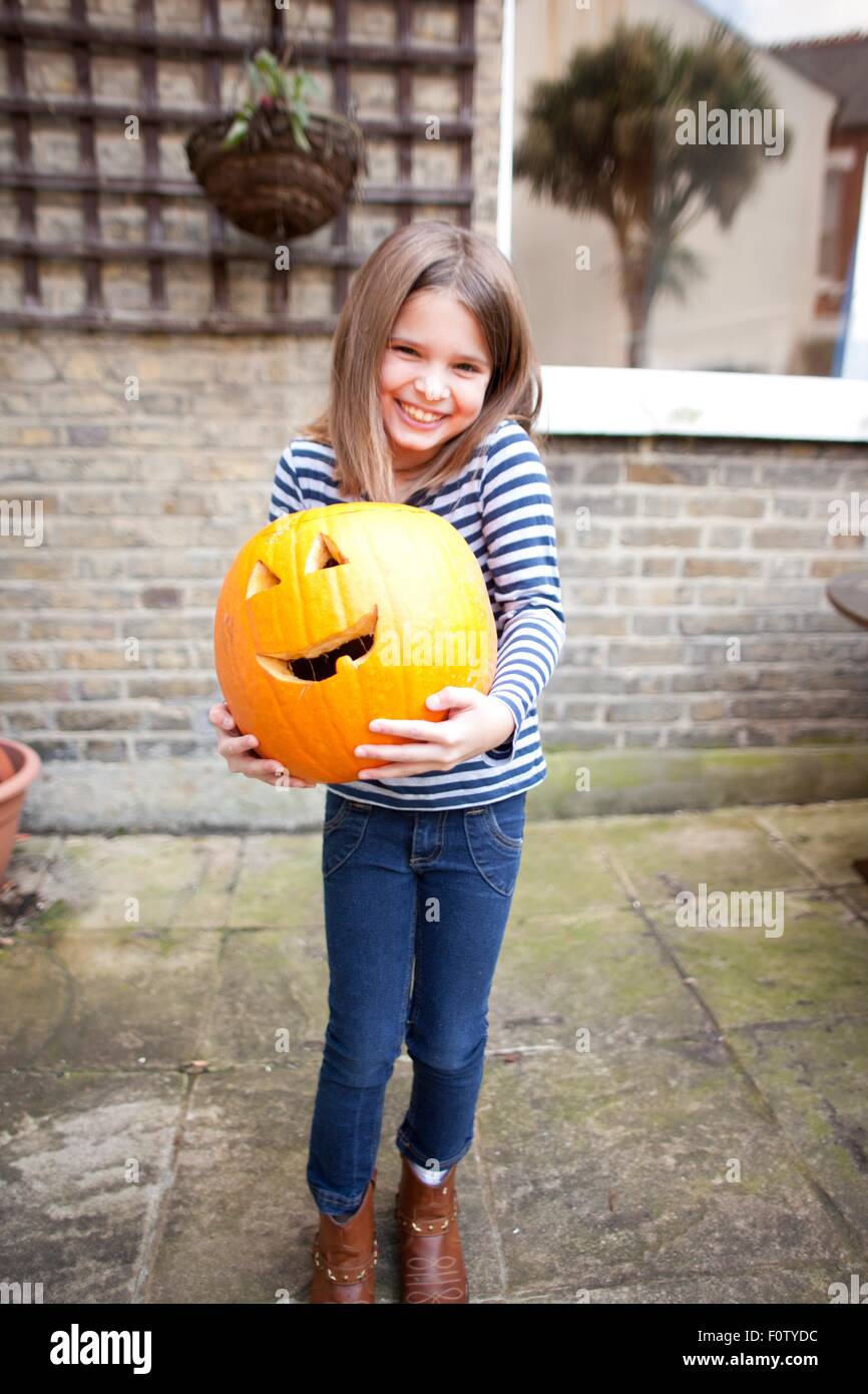 Lächelnde Mädchen halten schwere Halloween-Kürbis im Garten Stockfoto