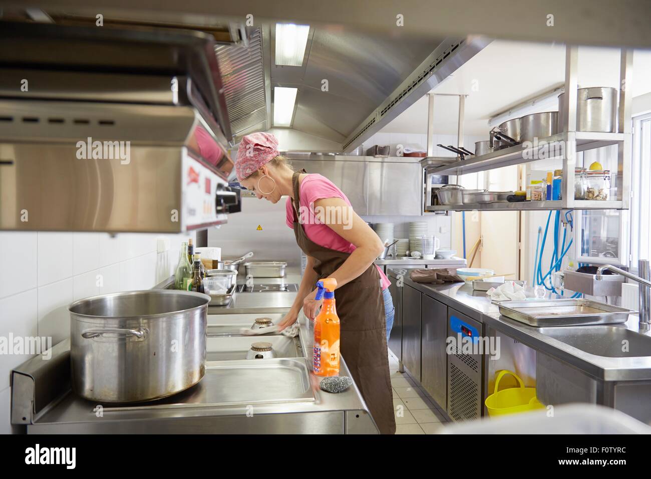 Reife Frau mit Schürze und Kopftuch Reinigung Küche Herd Stockfoto