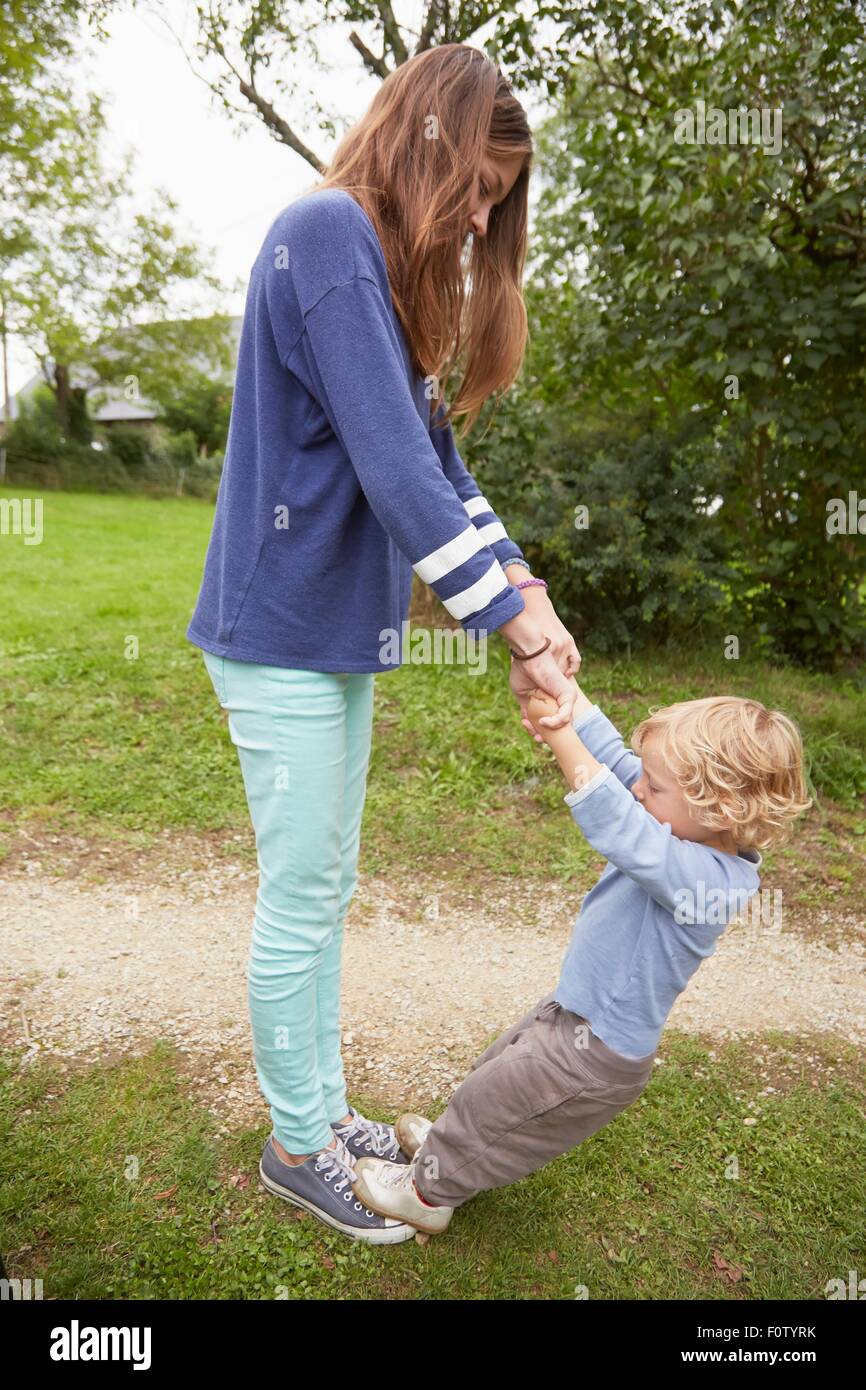 Teenager-Mädchen mit Kleinkind Bruder stehen auf ihren Füßen im Garten Stockfoto