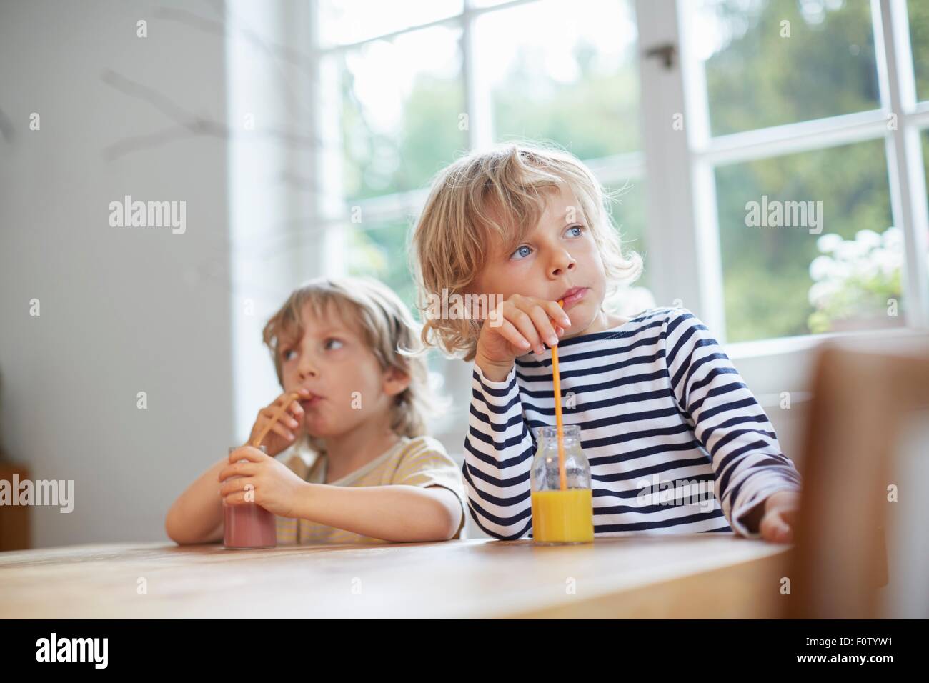 Zwei junge Brüder sitzen am Tisch trinken Getränke mit einem Strohhalm Stockfoto