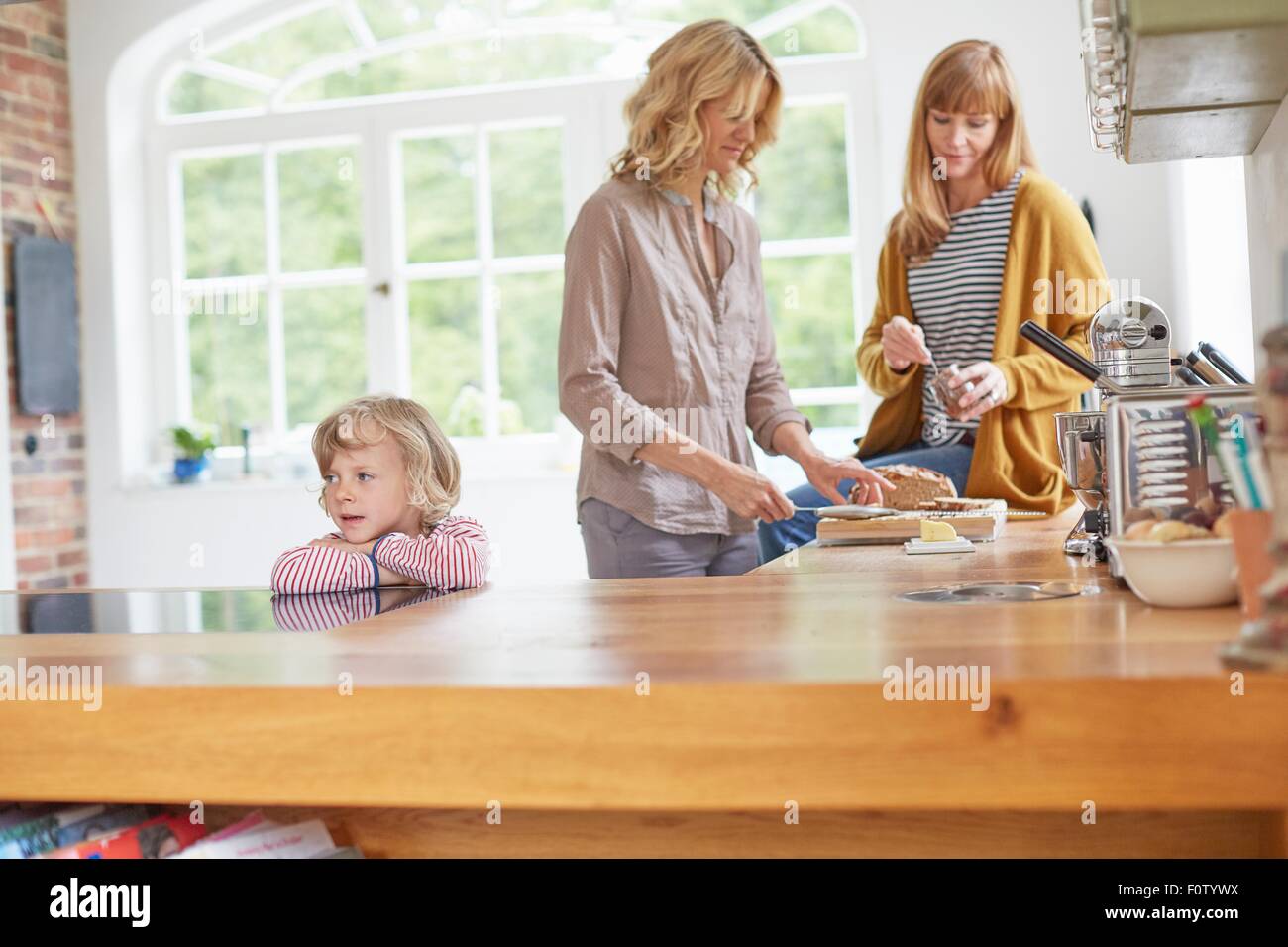 Zwei Frauen Zubereitung von Speisen in der Küche, während junge vom Küchentisch wartet Stockfoto