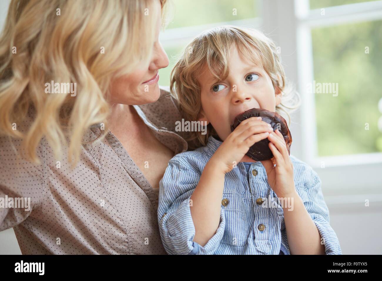 Schoko-Muffin zu sitzen, während seine Mutter auf eine blickt junge Stockfoto
