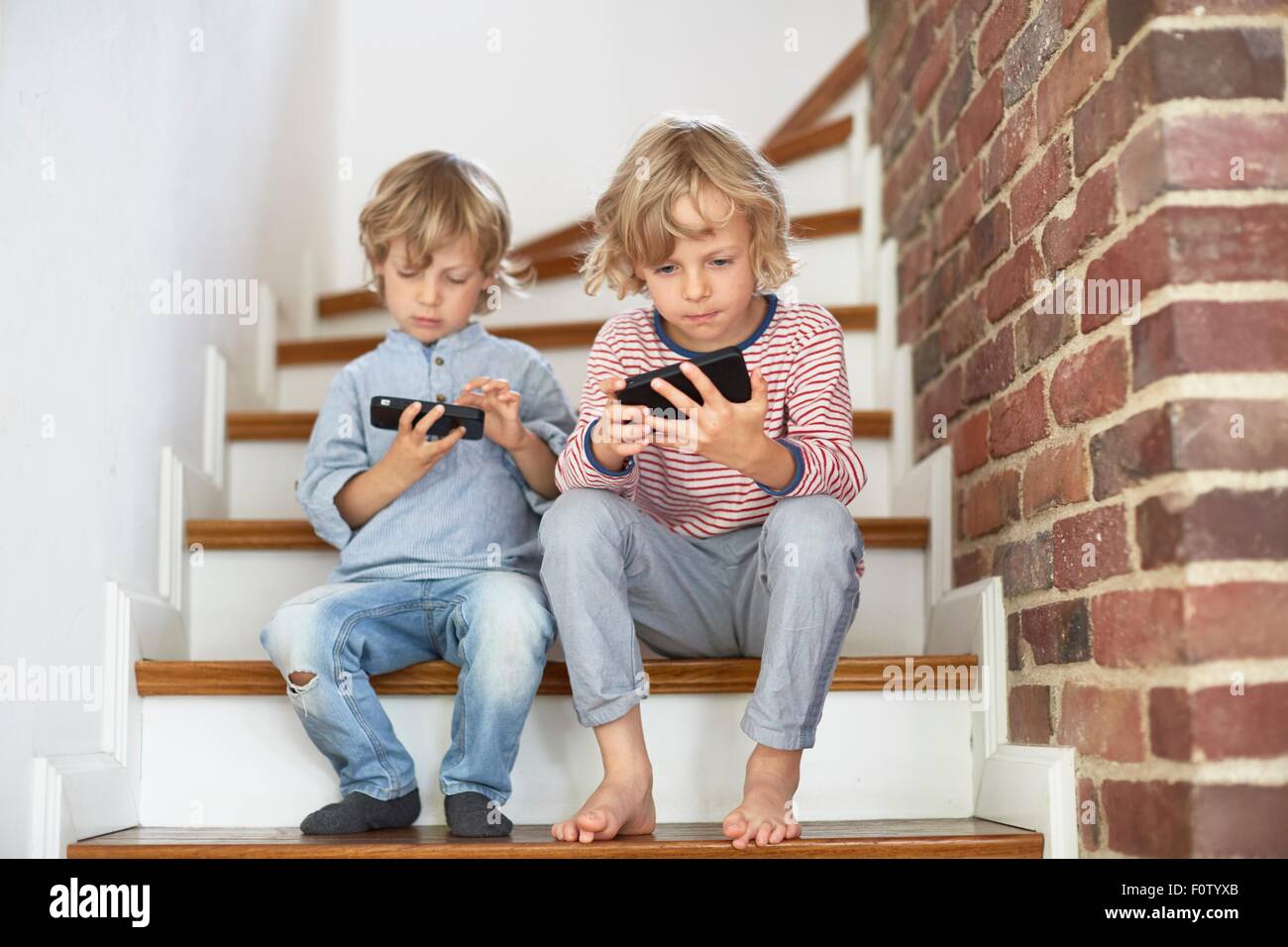 Zwei junge Brüder sitzen auf Treppe, Blick auf smartphones Stockfoto