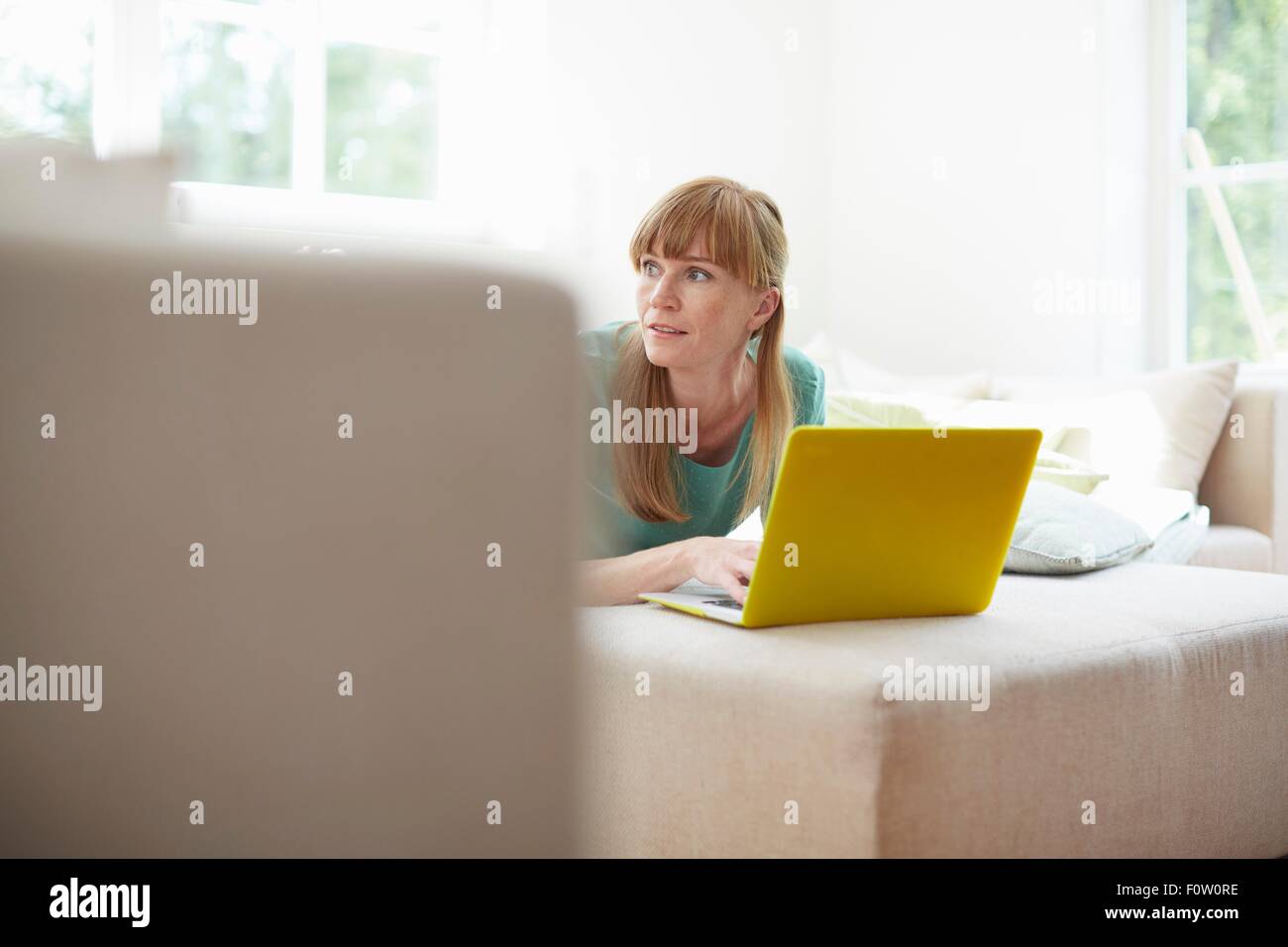 Mitte der erwachsenen Frau mit Laptop wegschauen Stockfoto