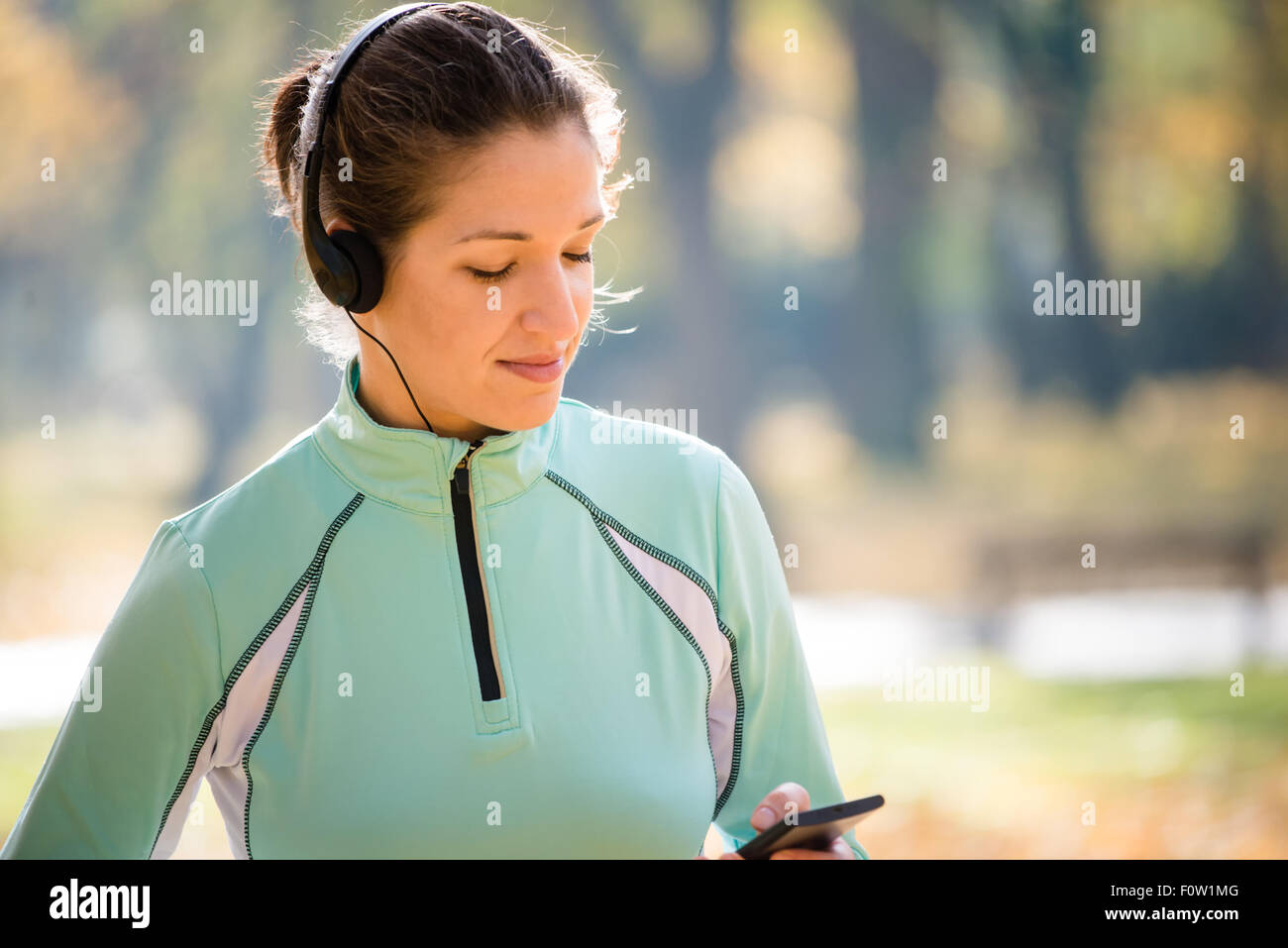 Junge Frau mit Kopfhörern in der herbstlichen Natur joggen und auf Handy Stockfoto