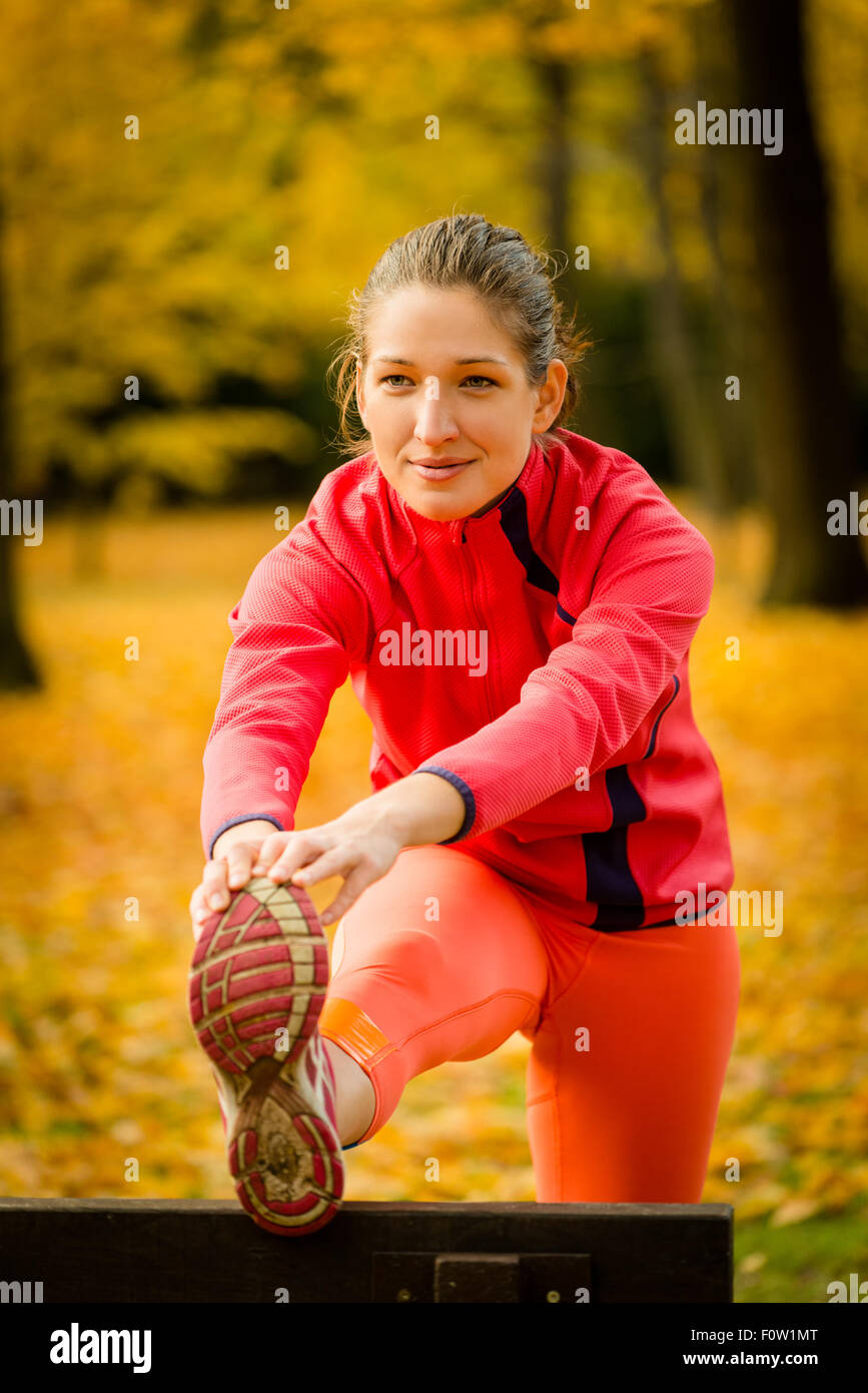 Junge Frau dehnen ihr Bein auf der Bank vor dem Joggen im Herbst Natur Stockfoto