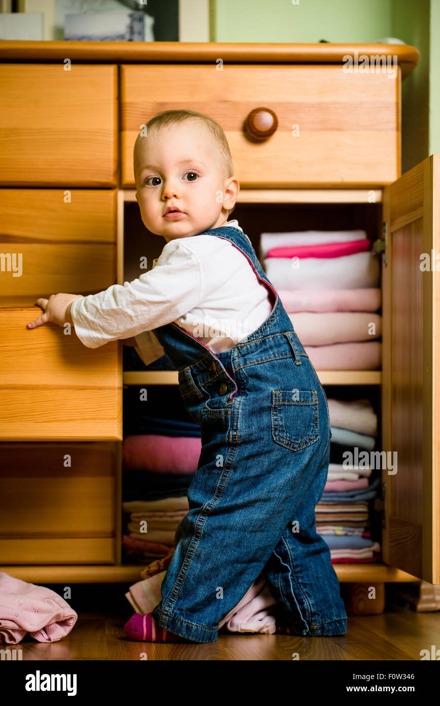 Baby wirft sich Kleider von Holzmöbeln zu Hause Stockfoto