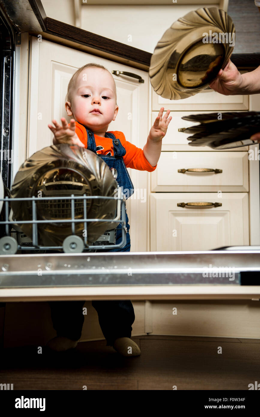 Niedliche Baby Mutter entladen Geschirrspüler in der Küche zu helfen Stockfoto