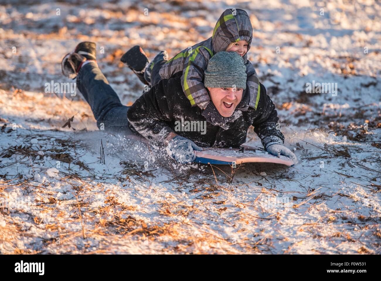 Porträt des Lächelns, Vater und Sohn Rodeln bergab im Schnee Stockfoto