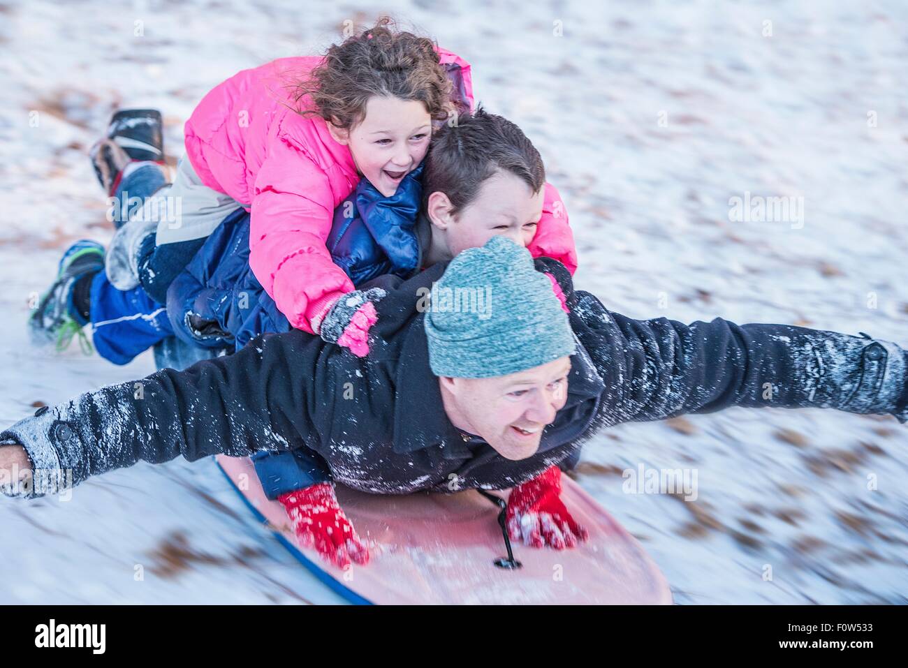 Porträt von Vater, Sohn und Tochter fahren Schlitten bergab übereinander legen Stockfoto