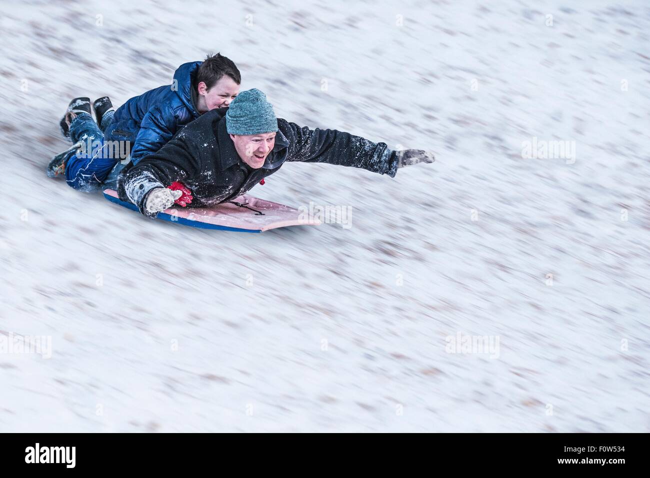 Vater und Sohn Rodeln bergab im Schnee Stockfoto