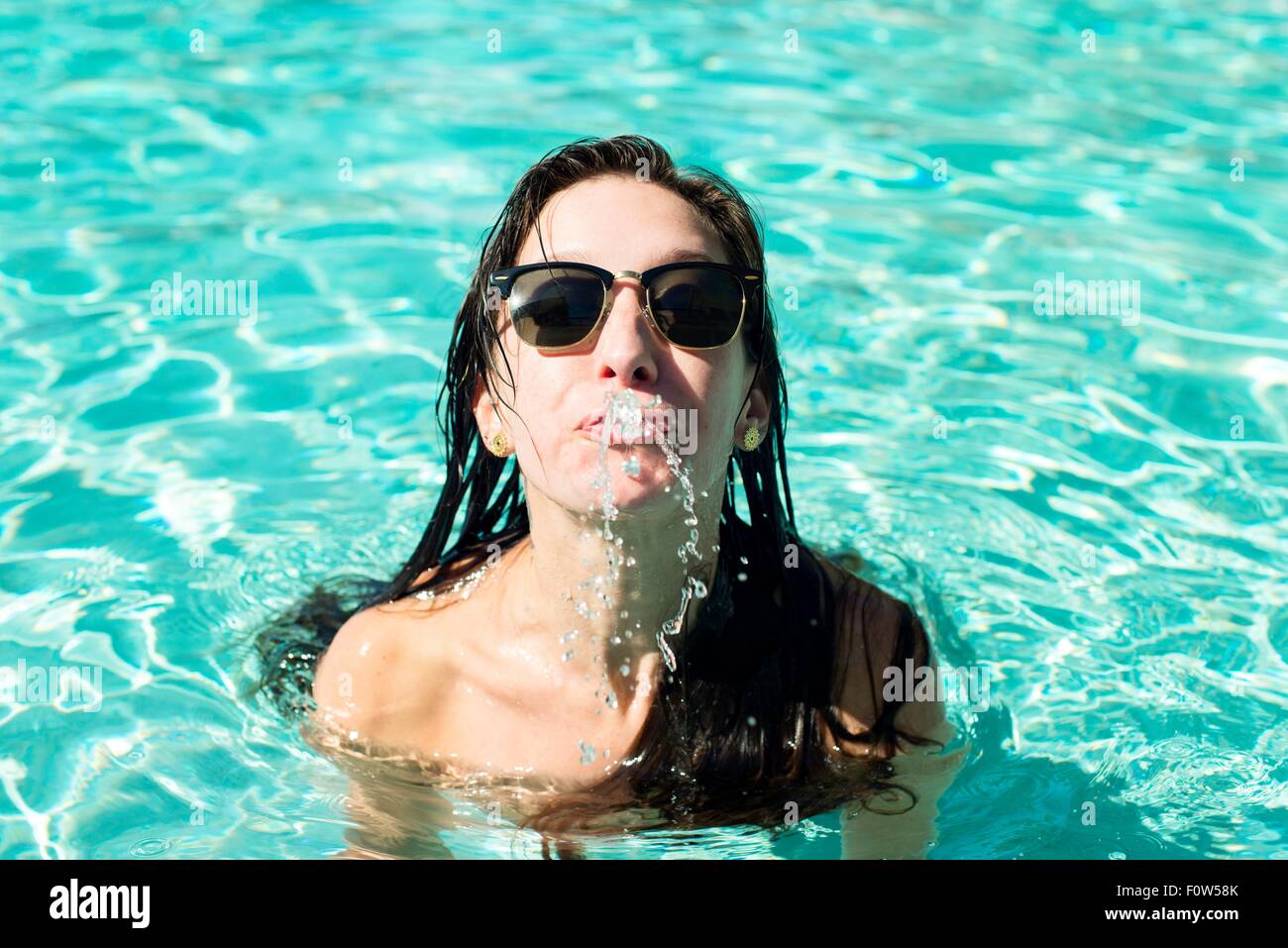 Porträt der jungen Frau im Schwimmbad Wasser aus Mund spritzen Stockfoto