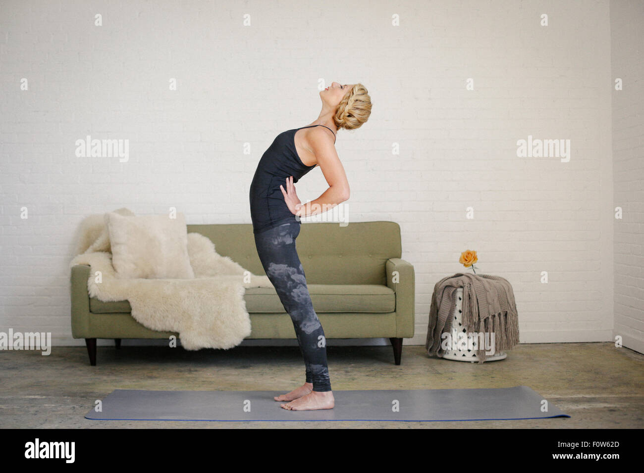Eine blonde Frau auf eine Yoga-Matte in einem Raum stehen, Yoga machen, biegen nach hinten mit den Händen an den Hüften. Stockfoto