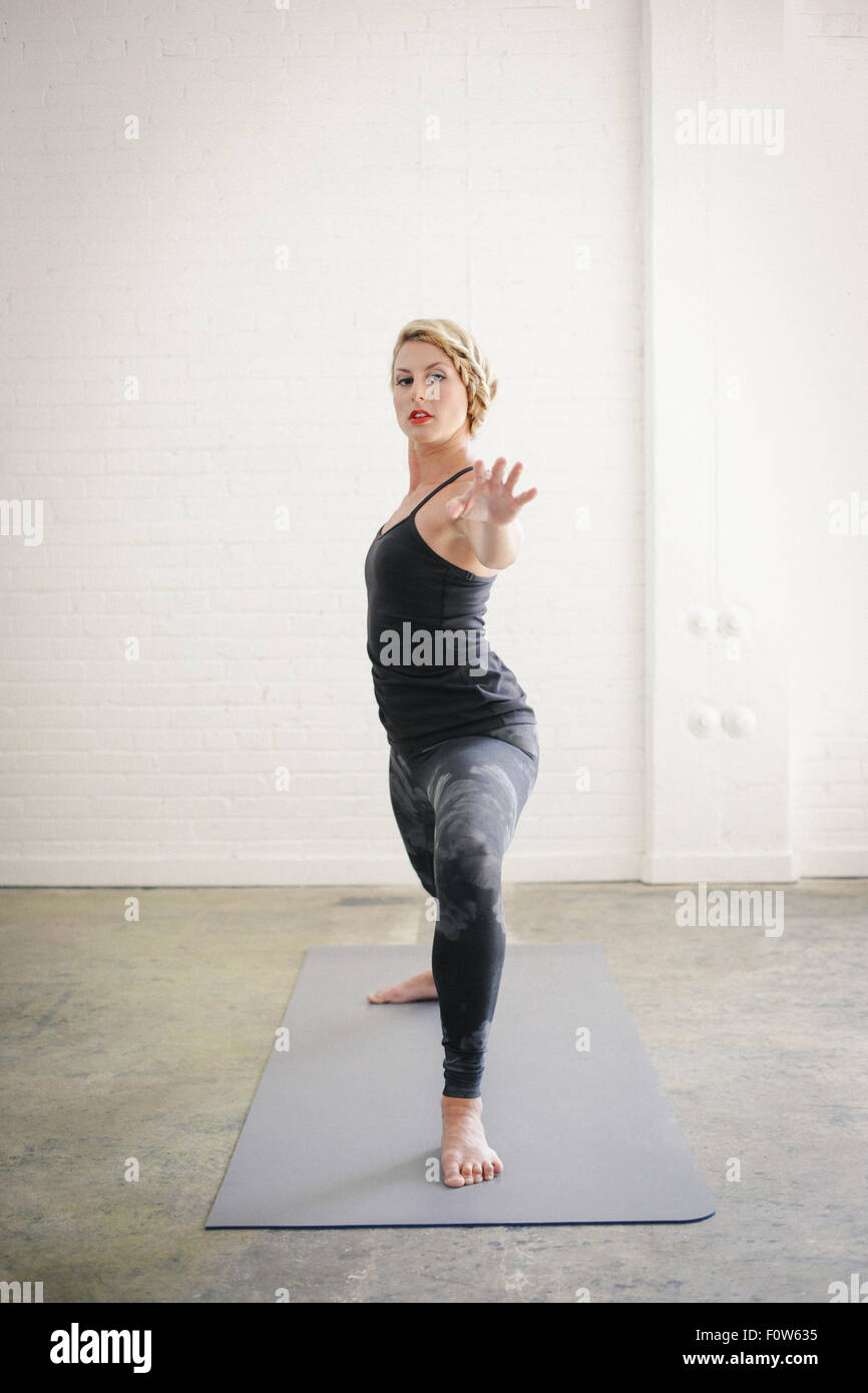 Eine blonde Frau in einem schwarzen Anzug und Leggings biegen Sie ihre Knie in einem Ausfallschritt mit ihren ausgestreckten Armen. Stockfoto