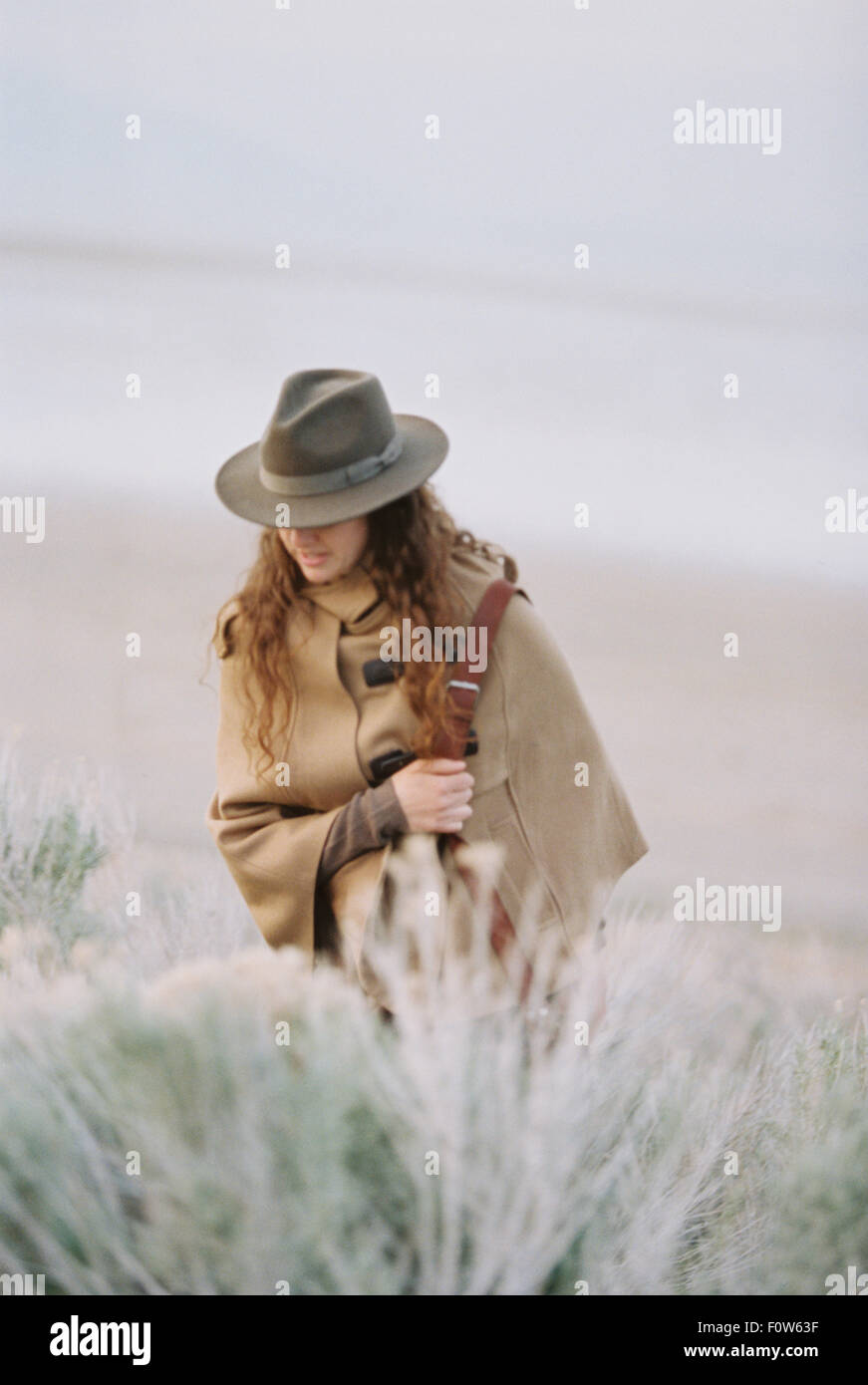 Eine Frau, ein Spaziergang durch ein Wüstenebene, Tasche trägt einen Hut und eine Leder tragen. Stockfoto