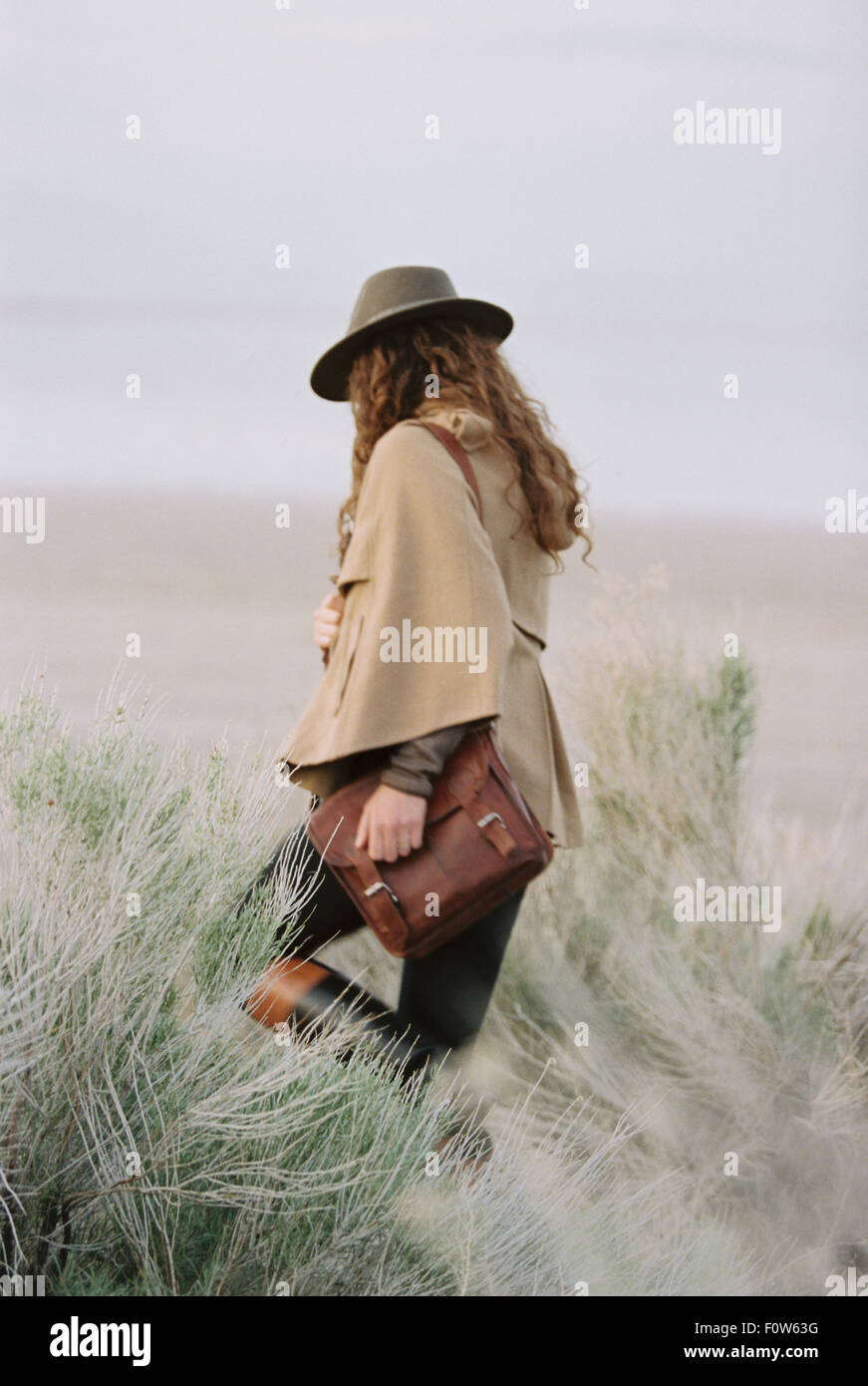 Frau zu Fuß durch eine Wüstenebene, einen Hut und eine Leder-Tragetasche. Stockfoto