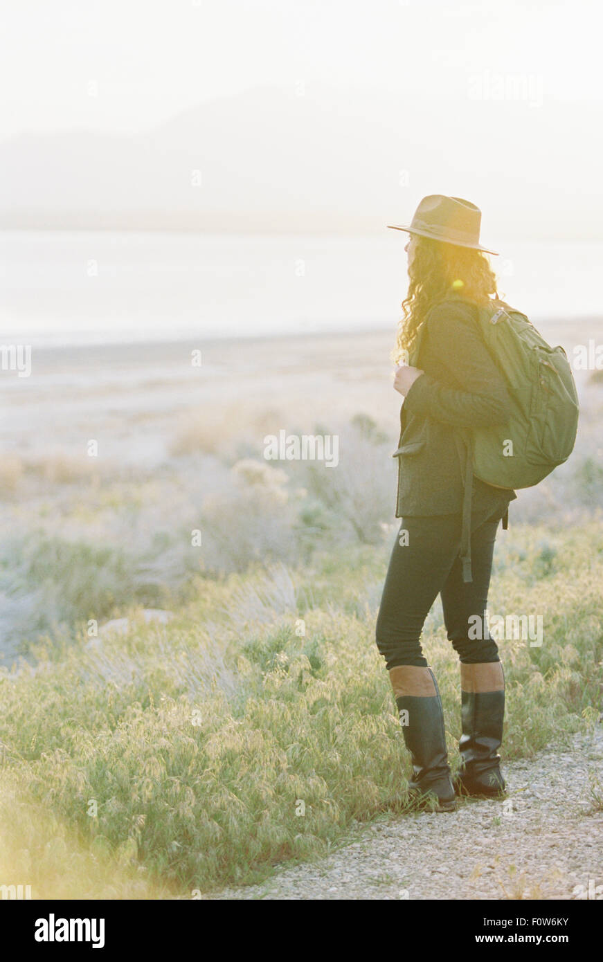 Eine Frau trägt einen Hut und Rucksack, stehend auf einem Weg mit Blick auf einen See und Tal. Stockfoto
