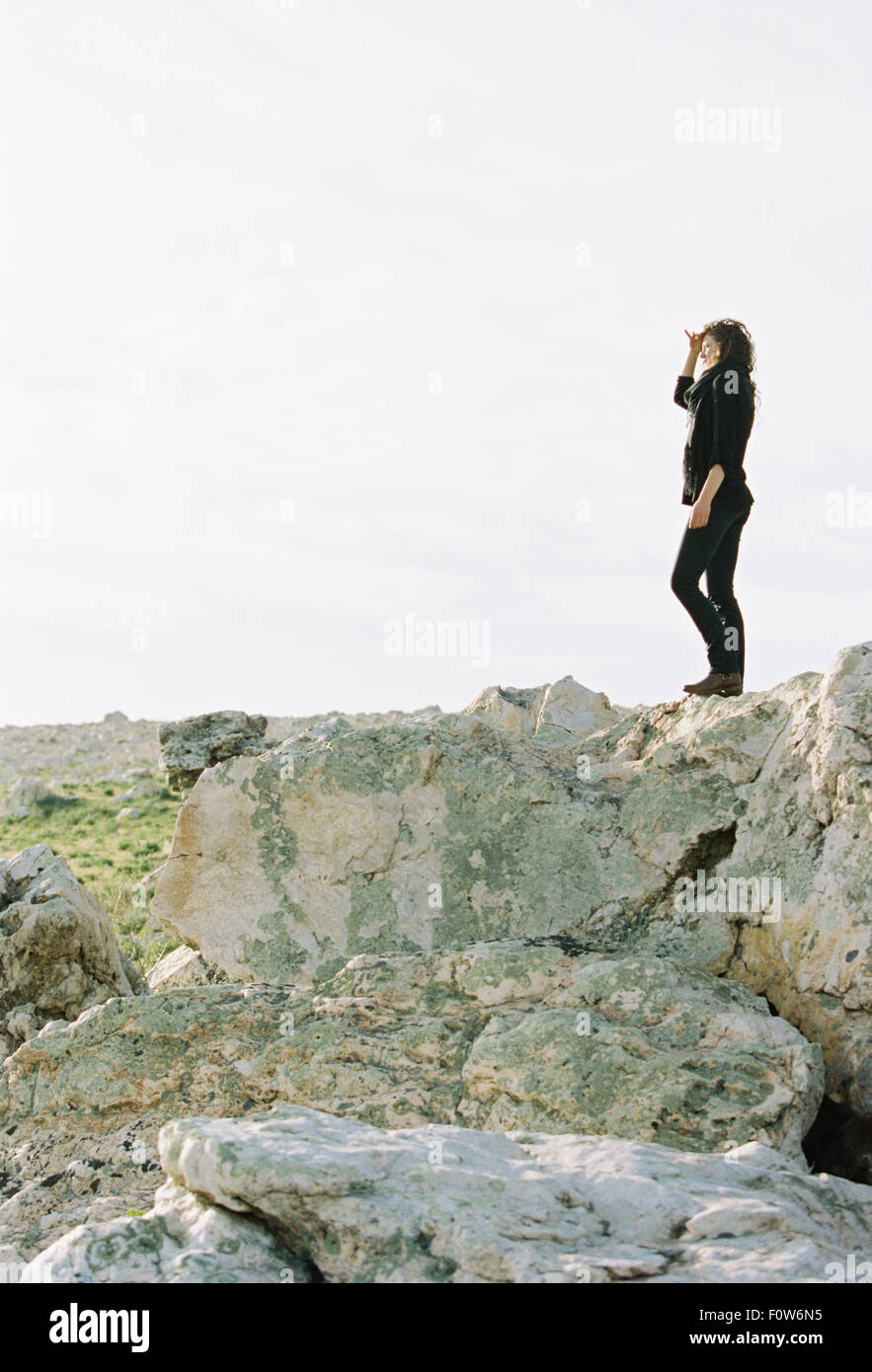 Eine Frau, die auf einem Felsen Abschirmung ihre Augen vor der Sonne mit der Hand. Stockfoto