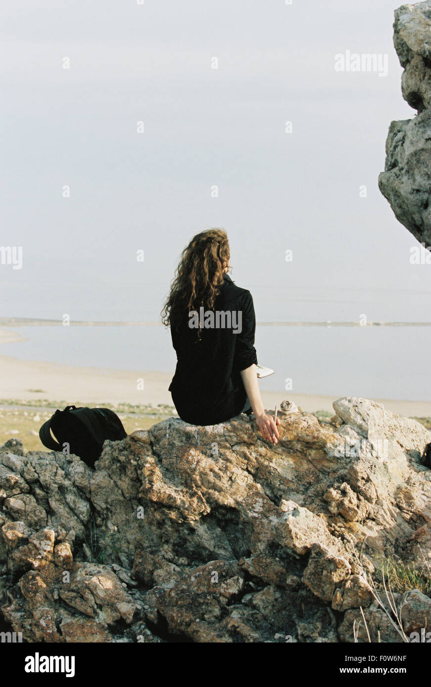 Eine Frau sitzt auf einem Felsen, Blick auf Wasser. Stockfoto