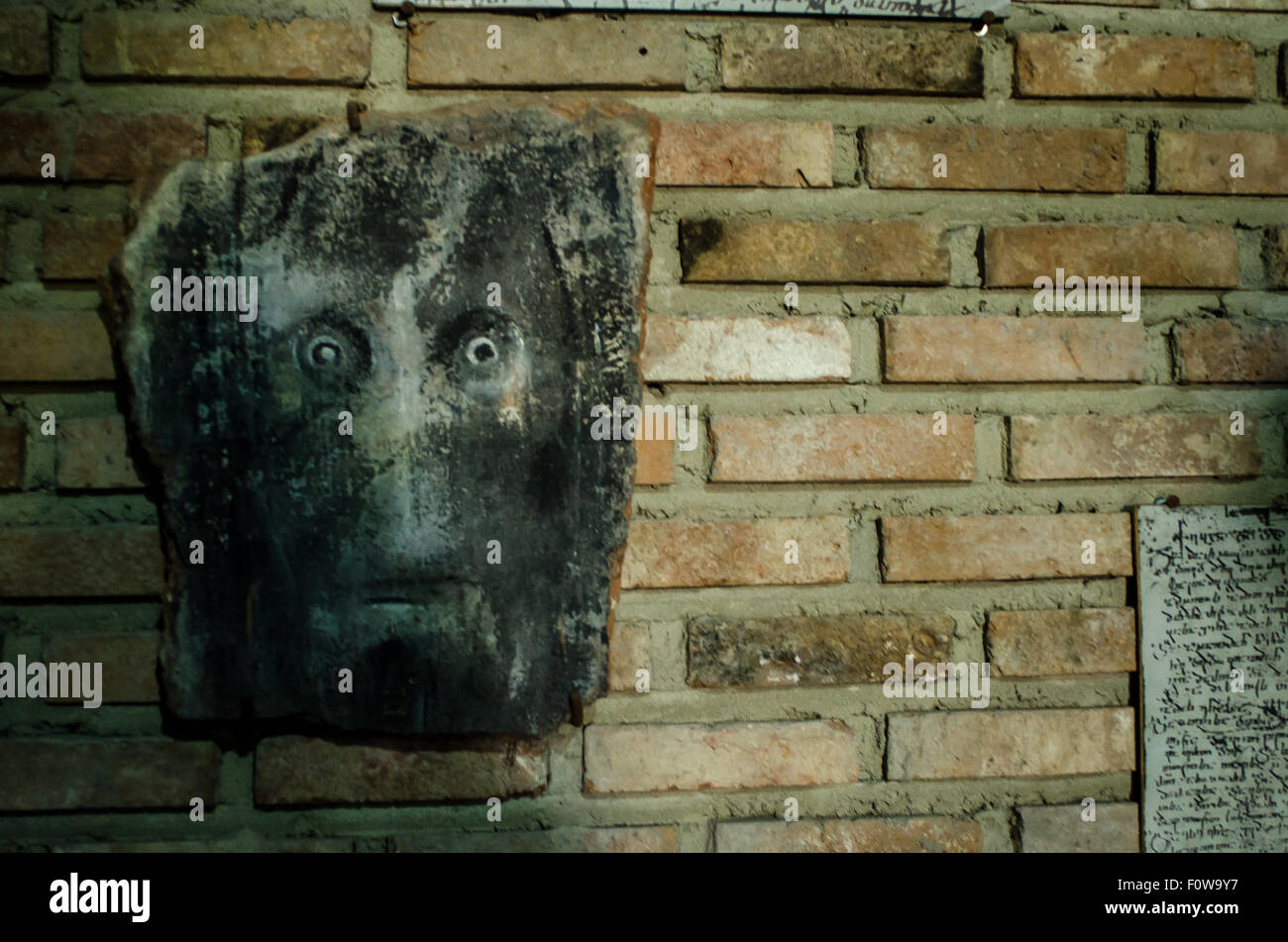 Faszinierende Steinmasken, die auf einer Backsteinmauer in einer historischen Stätte mit antiken Inschriften ausgestellt sind Stockfoto