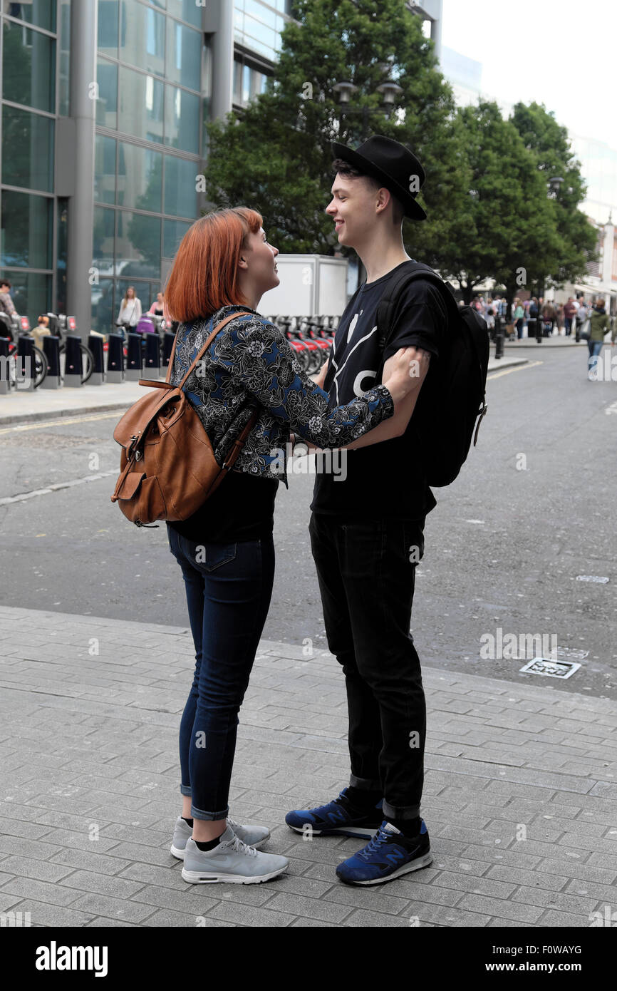 Ein trendiges junges, lächelndes Paar mit Rucksäcken, das im Sommer in der Brushfield Street Spitalfields Shoreditch East London UK KATHY DEWITT steht Stockfoto