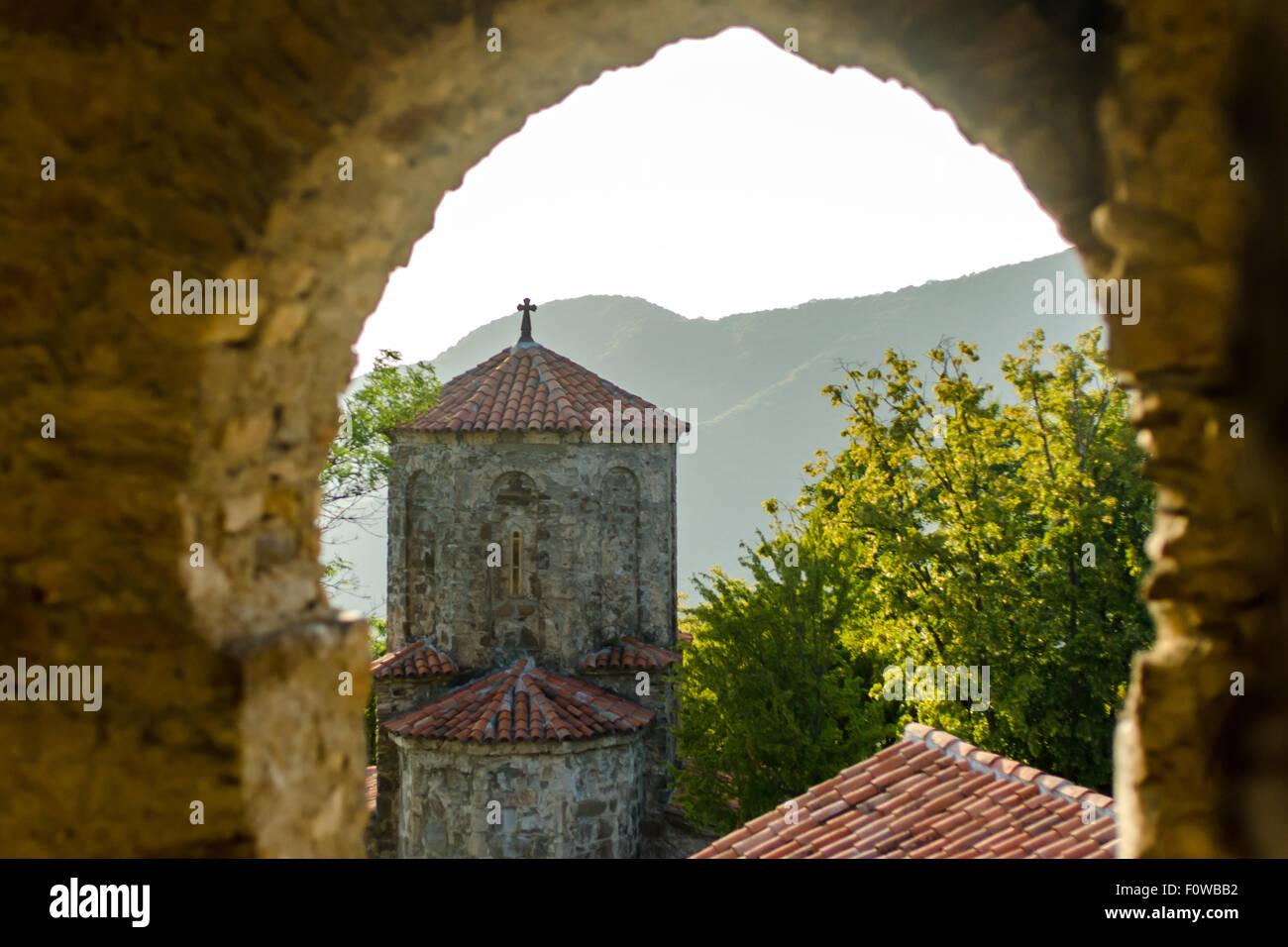 Historischer Kirchturm, eingerahmt von einem alten Steinbogen mit Bergen im Hintergrund während der goldenen Stunde Stockfoto