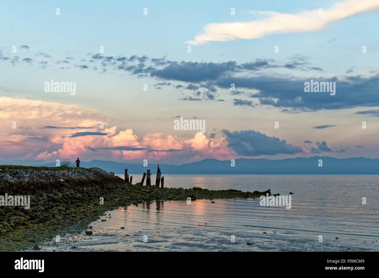 Ein Mann schaut zu, wie die Sonne im Hintergrund steigt. Die Sonne wird kurz und der Ebbe wird nach und nach Ende Stockfoto