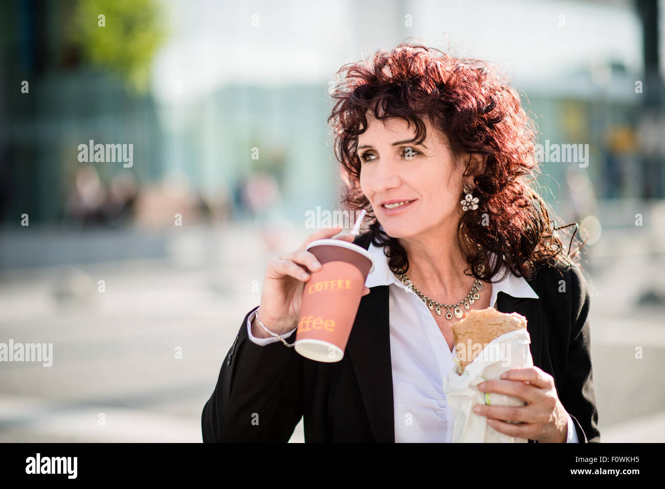 Senior Business-Frau, schnelle Mahlzeit im Street - Take-away-Kaffee trinken und Essen baguette Stockfoto