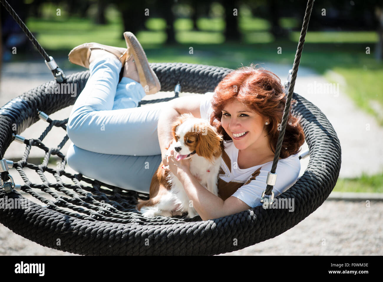 Reife Frau Schaukel mit ihrem cavalier Hund in Spielplatz im freien Stockfoto