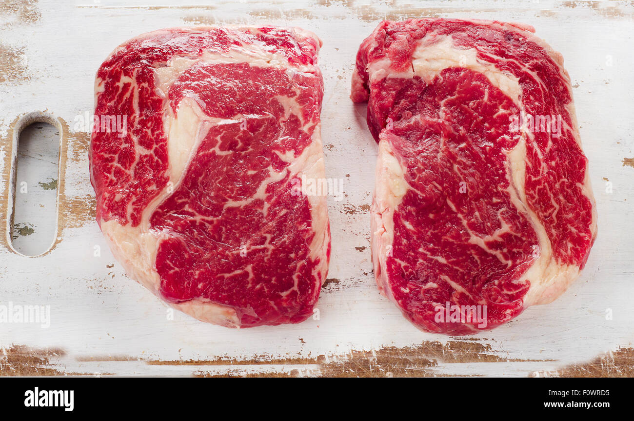 Rohe frische Ribeye-Steak auf einem weißen Holzbrett. Ansicht von oben Stockfoto