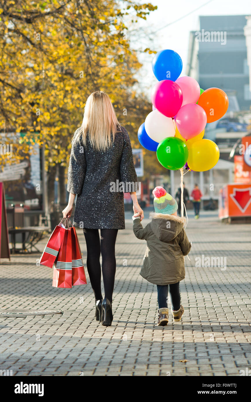 glückliche Frau und Kind mit roten Einkaufstasche und Luftballons, gehen auf der Straße Stockfoto