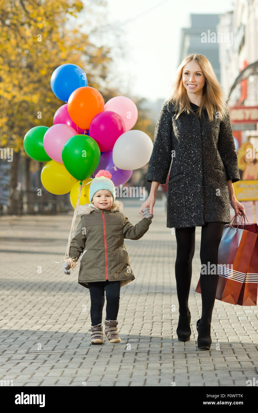 glückliche Frau und Kind mit roten Einkaufstasche und Luftballons, gehen auf der Straße Stockfoto