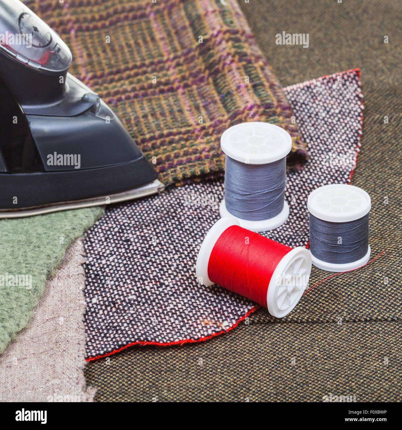 Schneiderei-Stillleben - Eisen und Thread Spulen auf Textil Bekleidung Stockfoto