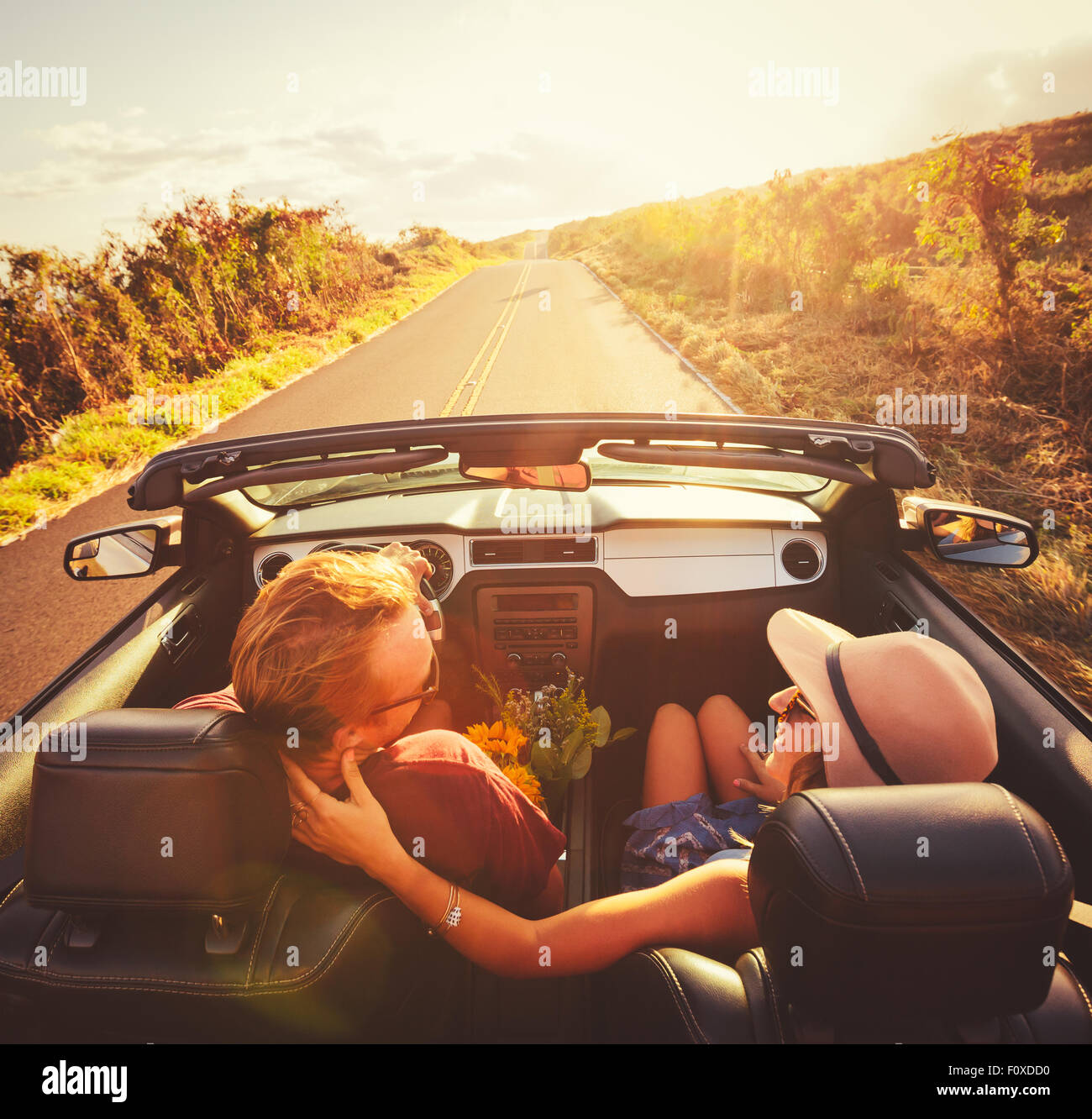Glückliches junges Paar Fahrt entlang der Landstraße im Cabrio bei Sonnenuntergang Stockfoto