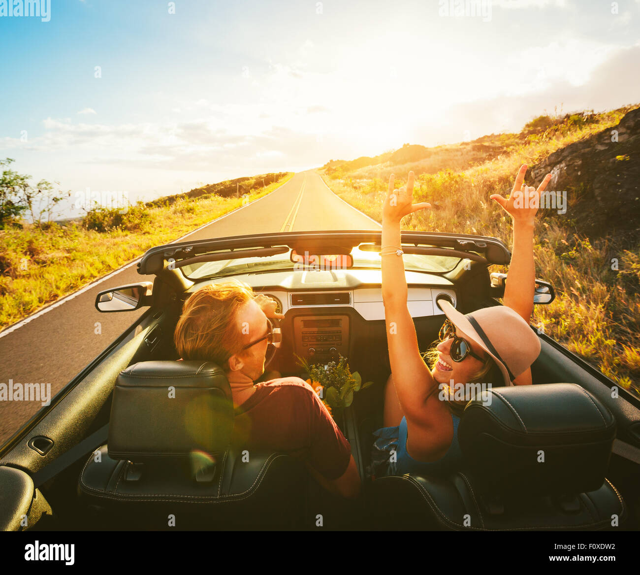Glückliche junge unbeschwerte paar Fahrt entlang der Landstraße im Cabrio bei Sonnenuntergang Stockfoto