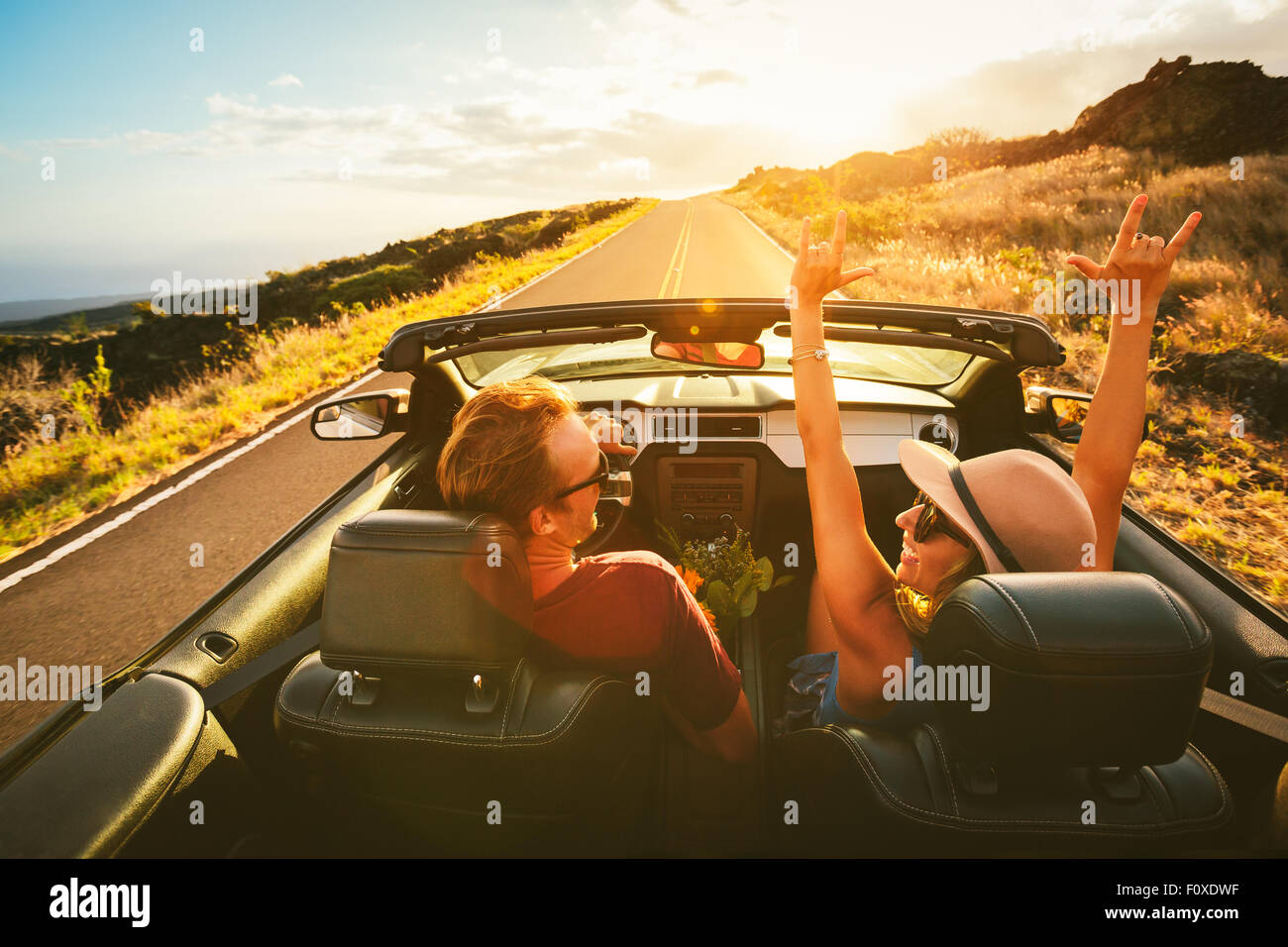Glückliche junge unbeschwerte paar Fahrt entlang der Landstraße im Cabrio bei Sonnenuntergang Stockfoto