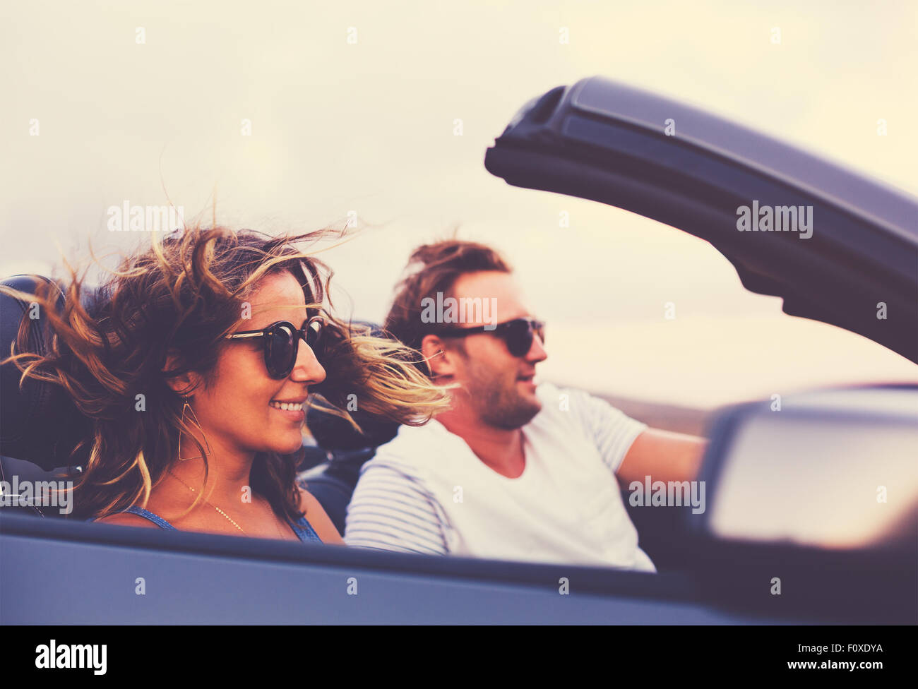 Glückliches junges Paar Fahrt entlang der Landstraße im Cabrio bei Sonnenuntergang Stockfoto