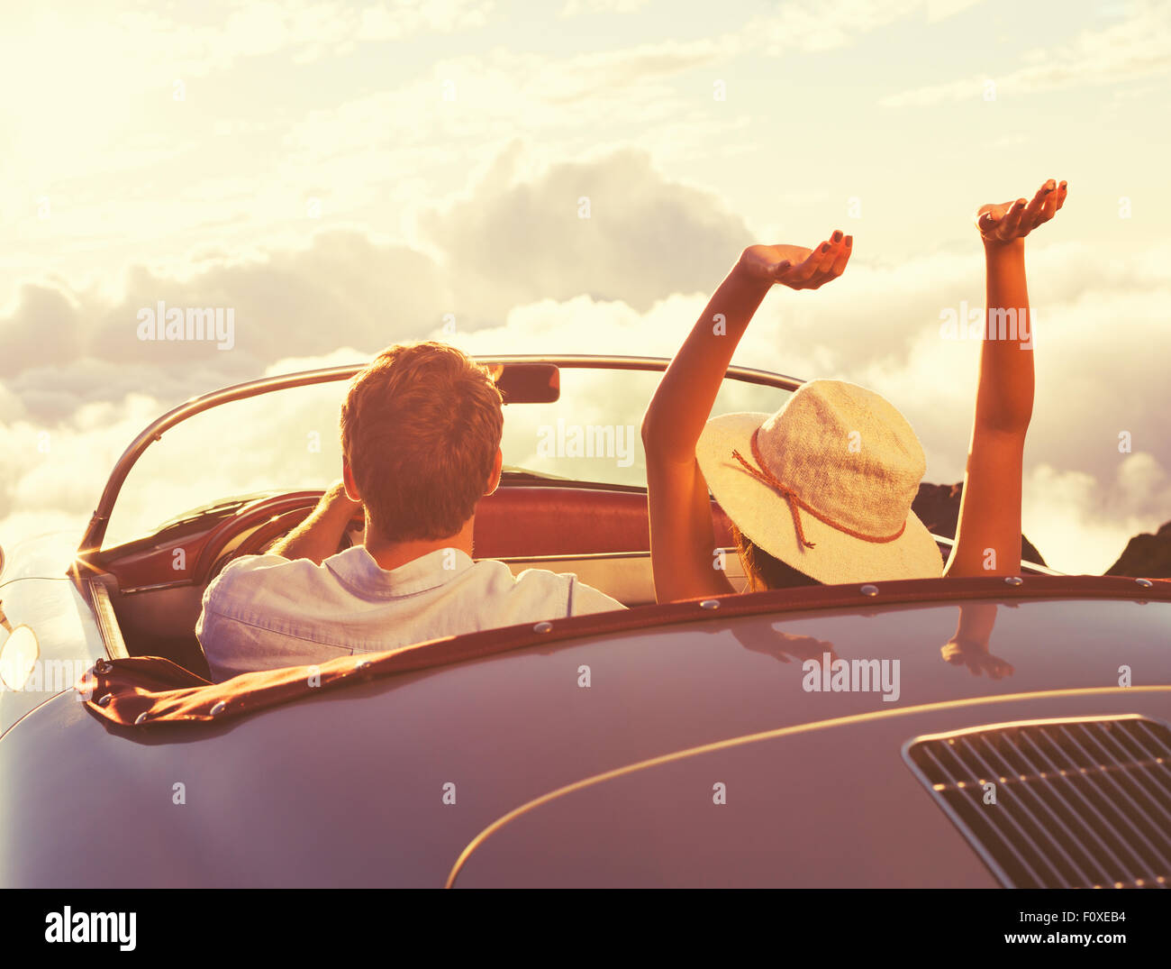 Fahrt in den Sonnenuntergang. Glückliches junges Paar genießen den Sonnenuntergang im klassischen Oldtimer Sportwagen. Stockfoto