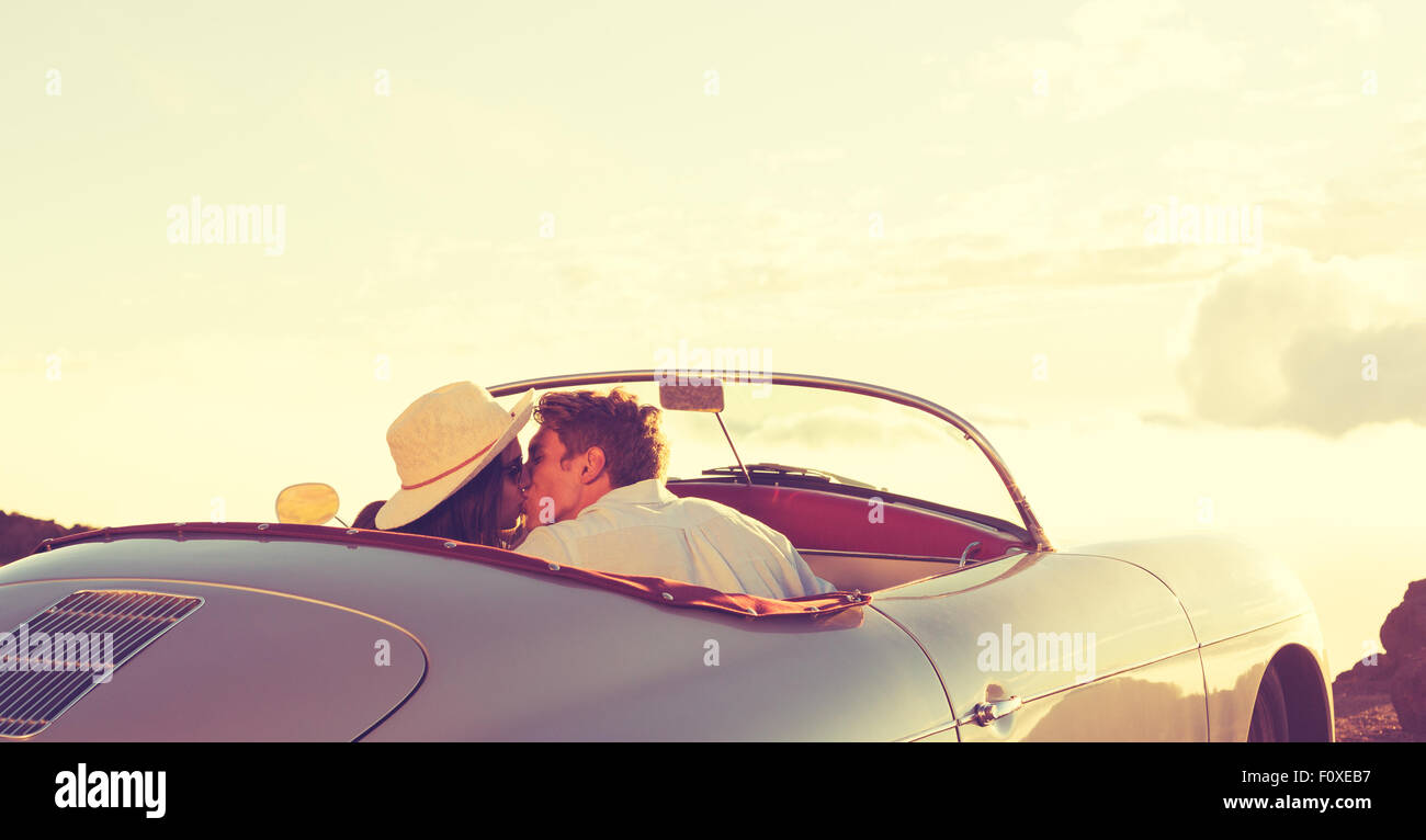 Romantische junges attraktives Paar den Sonnenuntergang beobachten und küssen im klassischen Oldtimer Sportwagen Stockfoto
