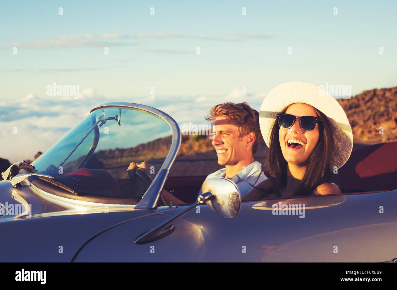 Glückliches junges Paar in klassischen Oldtimer Sportwagen bei Sonnenuntergang Stockfoto
