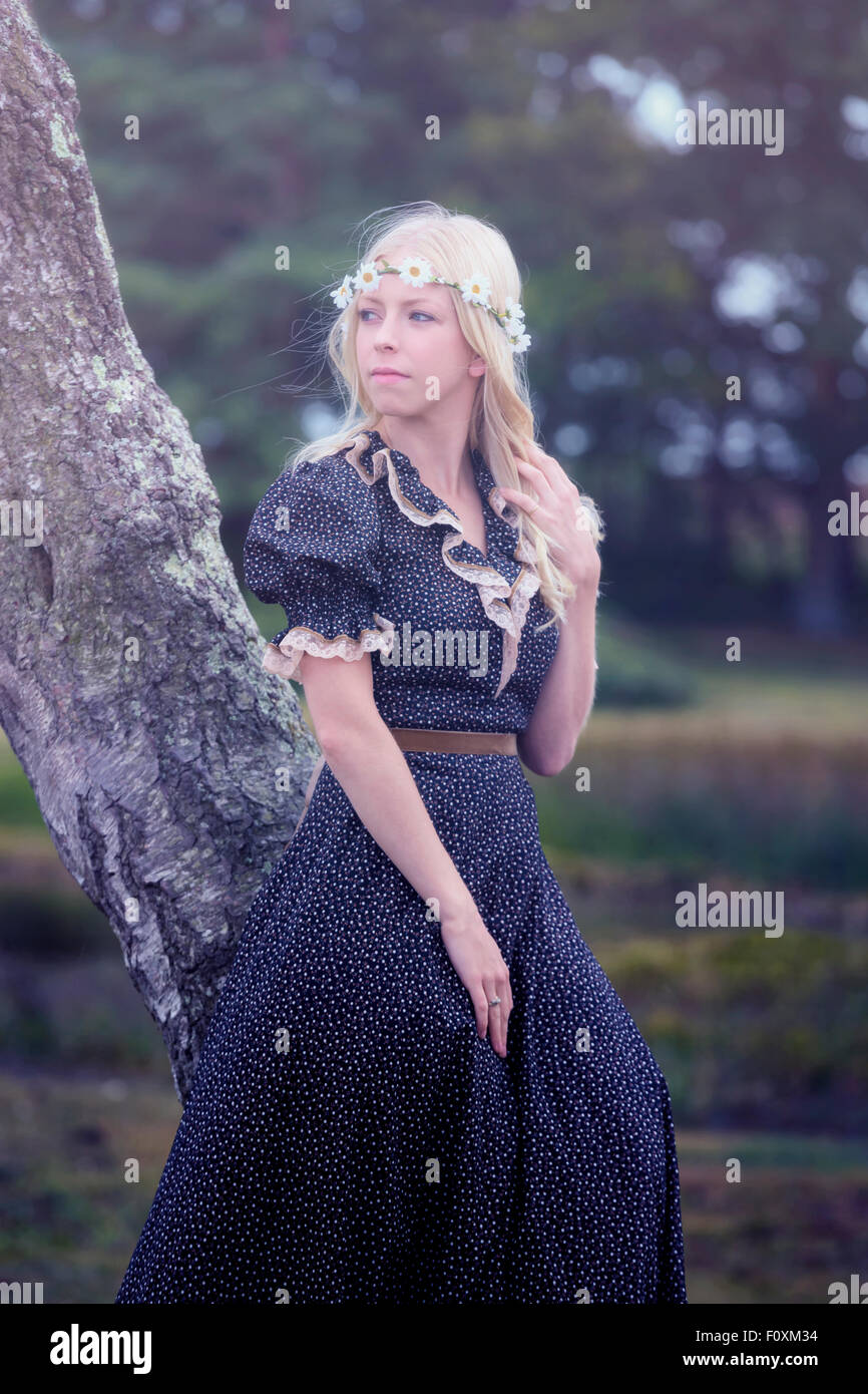 ein blondes Mädchen in einem floralen Dressl ist gegen einen Baum gelehnt. Stockfoto